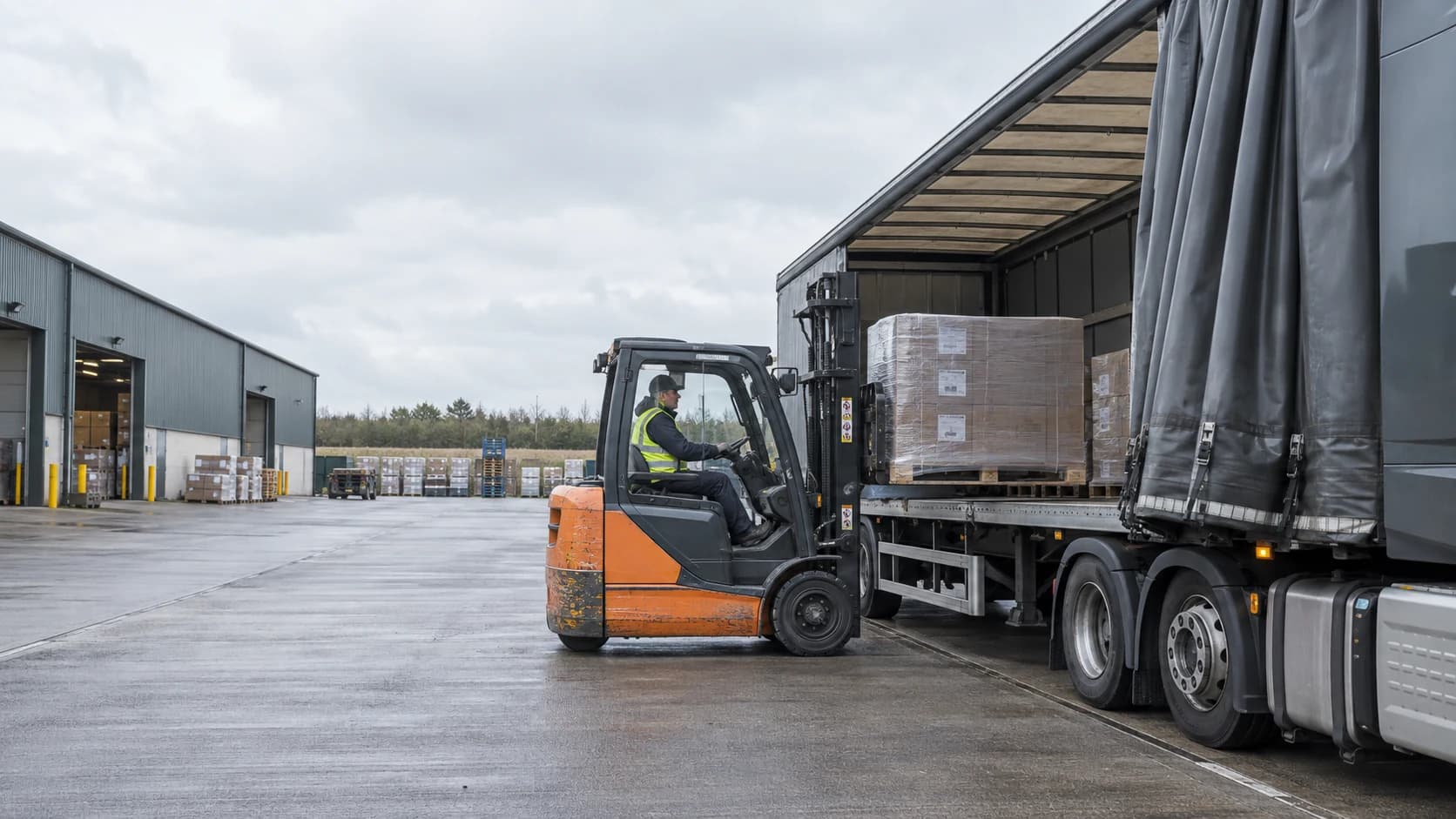 Forklift positioning a wrapped pallet beside an open curtainsider