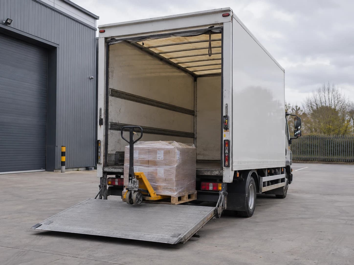 Wrapped pallet resting on a lowered truck tail-lift at a delivery forecourt